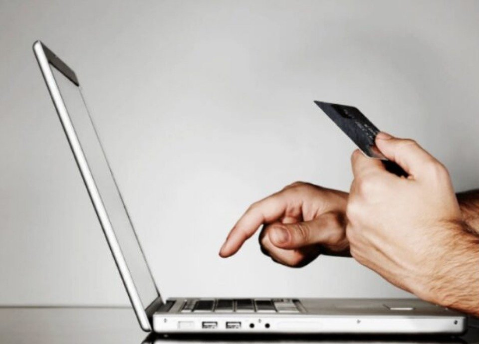 #descriçãodaimagem: Foto de uma pessoa com uma das mãos clicando no teclado de um laptop e a outra segurando o celular. Fim da descrição.
