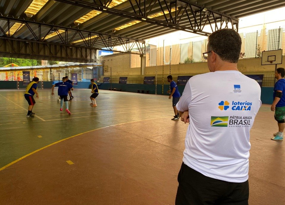 #descriçãodaimagem: Foto do treino de Futsal com os atletas surdos da CBDS. Em primeiro plano está o técnico da Seleção Brasileira, que observa os atletas durante o treino na quadra. Fim da descrição.