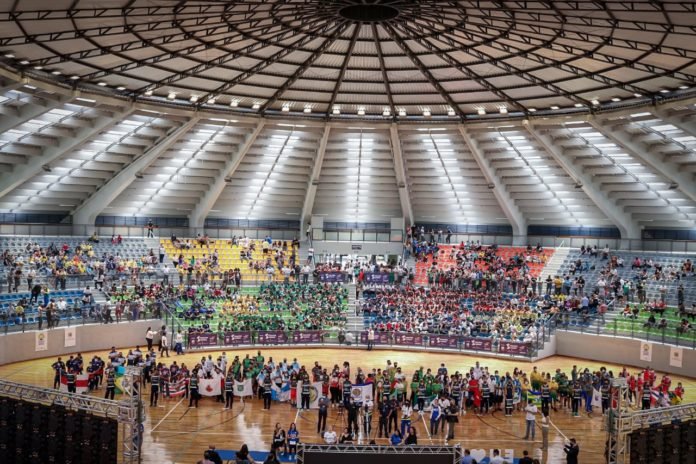 #descriçãodaimagem: foto geral do ginásio durante a abertura do evento. Fim da descrição.