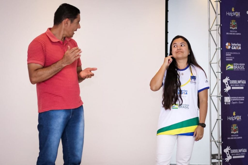 #descriçãodaimagem: foto do secretário Guedes com a presidente da CBDS, Diana Kyosen, durante o encontro. Eles estão no palco e conversam em Libras. Fim da descrição.