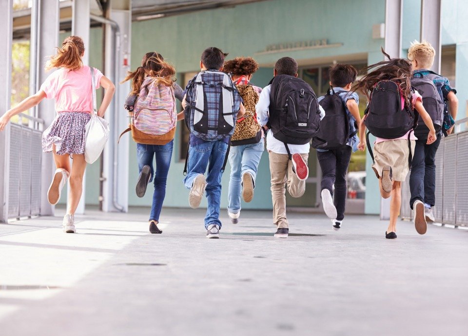 #descriçãodaimagem foto de várias crianças correndo com mochilas nas costas. Fim da descrição.