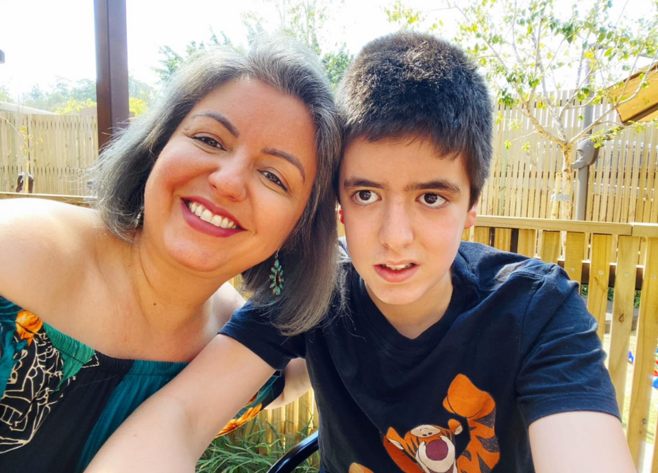 #descriçãodaimagem Foto de Andrea Werner com o filho Theo. Andrea é uma mulher branca de cabelos castanhos, na altura dos ombros. Theo é um jovem branco de cabelos pretos curtos. Eles estão lado a lado e sorriem. Fim da descrição.