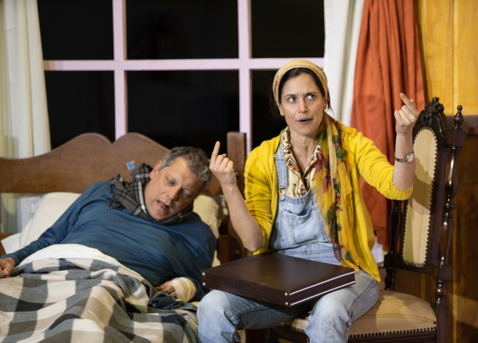 #descriçãodaimagem #pratodosverem foto de uma cena da peça Misery. Na cena estão dois atores. Um homem, deitado em uma cama, enquanto tenta se levantar. E uma mulher, que está sentada em uma cadeira, ao lado da cama.