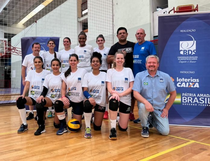 Descrição da imagem: Foto das atletas de vôlei com membros da comissão técnica. Fim da descrição.
