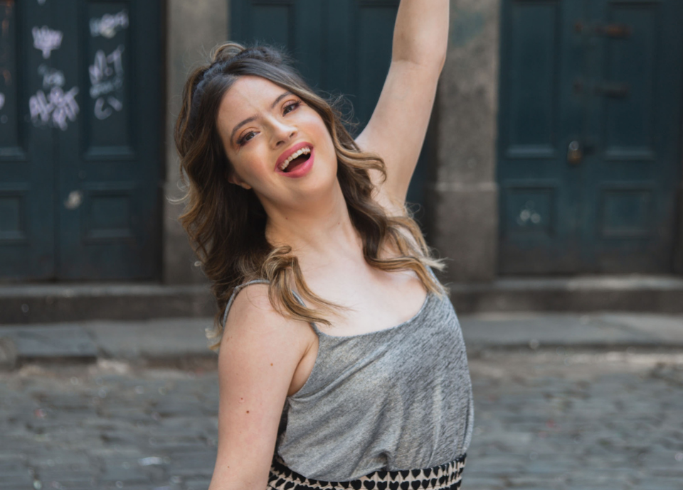 #descriçãodaimagem Foto da influenciadora Samanta Quadrado. Ela é morena, tem pele clara, e cabelos longos, castanhos, com luzes. Ela está usando um vestido cinza. Fim da descrição.