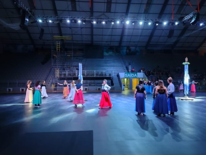 Descrição da imagem: foto dos artistas durante o ensaio do espetáculo que será apresentado na cerimônia de abertura da Summer Deaflympics. Várias pessoas estão no ginásio. Elas estão usando roupas coloridas. Fim da descrição.