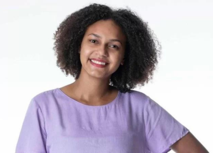 Descrição da imagem: Foto da professora Jessilane. Ela é uma mulher negra de cabelos castanhos e cacheados na altura dos ombros. Jessi está vestindo uma blusa lilás e sorri. Fim da descrição.