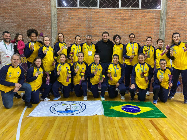 Descrição da imagem: foto das atletas e membros da comissão técnica da seleção de handebol feminino com a medalha de bronze. Fim da descrição.