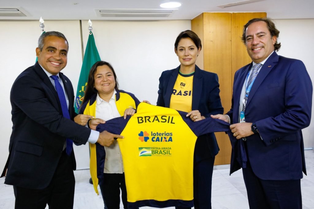 Descrição da imagem: foto da presidente da CBDS, Diana Kyosen com o ministro da Cidadania, Ronaldo Bento, a primeira-dama Michelle Bolsonaro e o presidente da Caixa, Pedro Guimarães. Eles seguram o uniforme do Brasil. Fim da descrição.