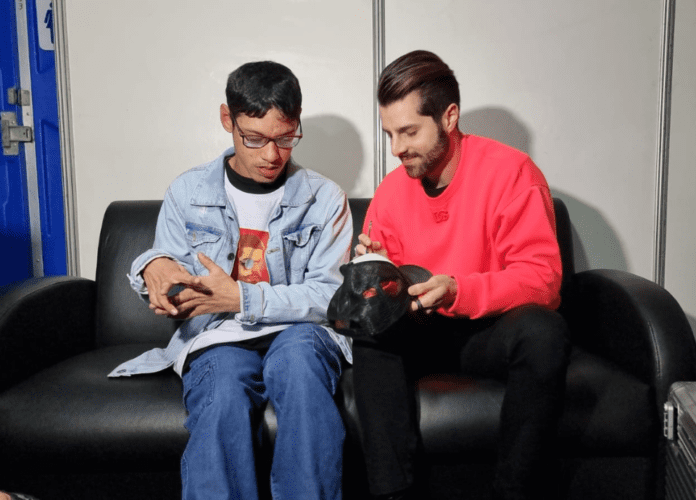Descrição da imagem: foto de João Pedro e Alok. Eles estão sentados, lado a lado, em um sofá preto, e conversam. Fim da descrição.