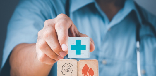 Descrição da imagem: foto de um médico empilhando cubos com ilustrações que remetem à saúde, como seringas, tubos de ensaio e uma cruz azul, entre outros. Fim da descrição.