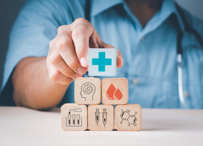 Descrição da imagem: foto de um médico empilhando cubos com ilustrações que remetem à saúde, como seringas, tubos de ensaio e uma cruz azul, entre outros. Fim da descrição.
