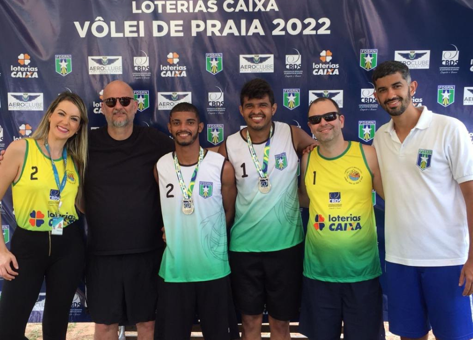 Descrição da imagem: foto dos medalhistas do campeonato de vôlei de praia, durante a premiação. Fim da descrição.