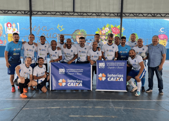 Descrição da imagem: foto dos atletas da Seleção Brasileira de Futsal Master de Surdos da CBDS. Eles estão perfilados e seguram o banner do patrocinador: Loterias Caixa. Fim da descrição.