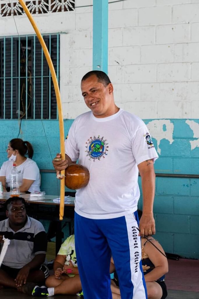 Descrição da imagem: foto do capoeirista Mestre Nei. Ele está em pé e segura seu berimbau. Fim da descrição.
