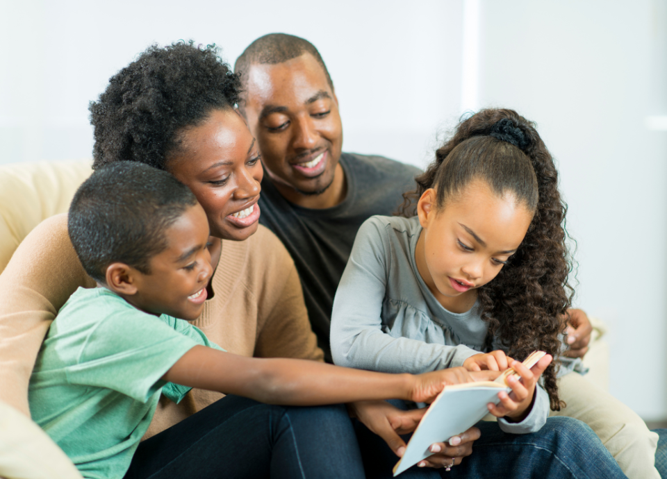 Descrição da imagem: foto de uma família, pai, mãe d dois filhos. Eles estão sentados lendo um livro, juntos. Fim da descrição.