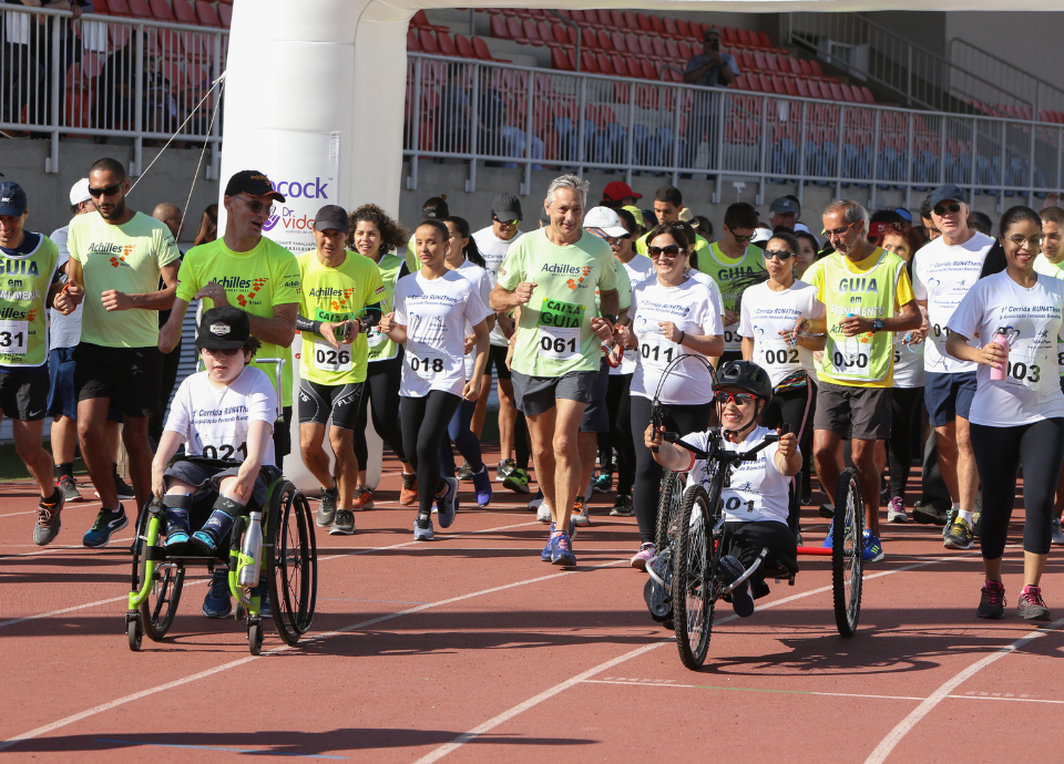 Descrição da imagem: foto de um grupo de participantes da 1ª edição da Corrida dos Sonhos. Eles estão na pista de atletismo do CT Paralímpico. Fim da descrição.