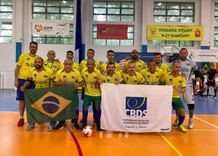 Descrição da imagem: foto dos surdoatletas da Seleção Brasileira Master de Futsal de Surdos. Eles estão perfilados e seguram as bandeiras do Brasil e da CBDS. Fim da descrição.