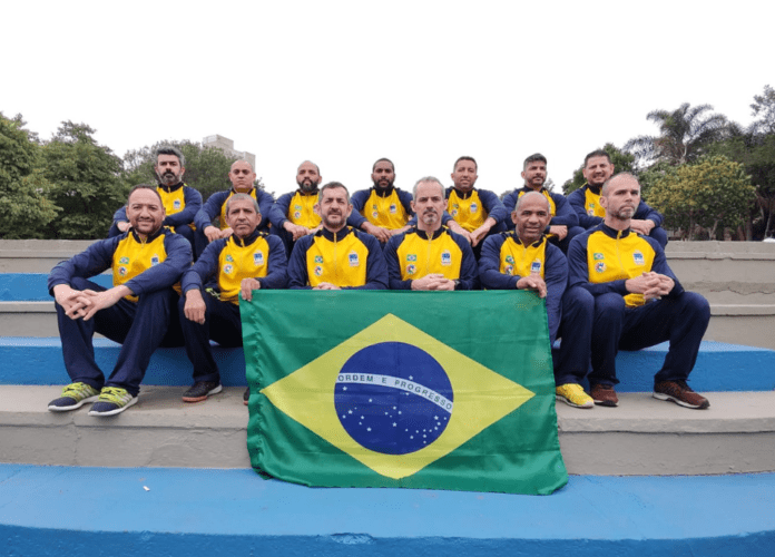 Descrição da imagem: foto dos surdoatletas da Seleção Brasileira Master de Futsal de Surdos. Eles estão segurando a bandeira do Brasil. Fim da descrição.