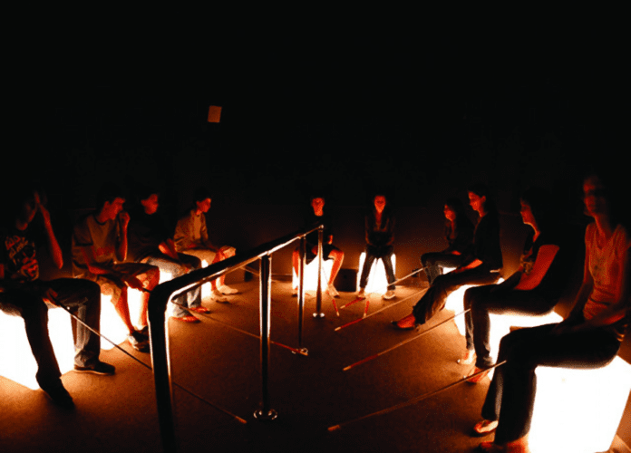 Descrição da imagem: foto de um grupo de pessoas sentadas em pufes iluminados. As pessoas estão segurando bengalas brancas. Fim da descrição.