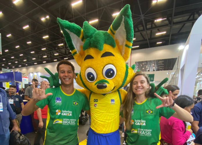 Descrição da imagem: foto dos atletas Romailson e Stefany com Lobin, o mascote da CBDS. Fim da descrição.