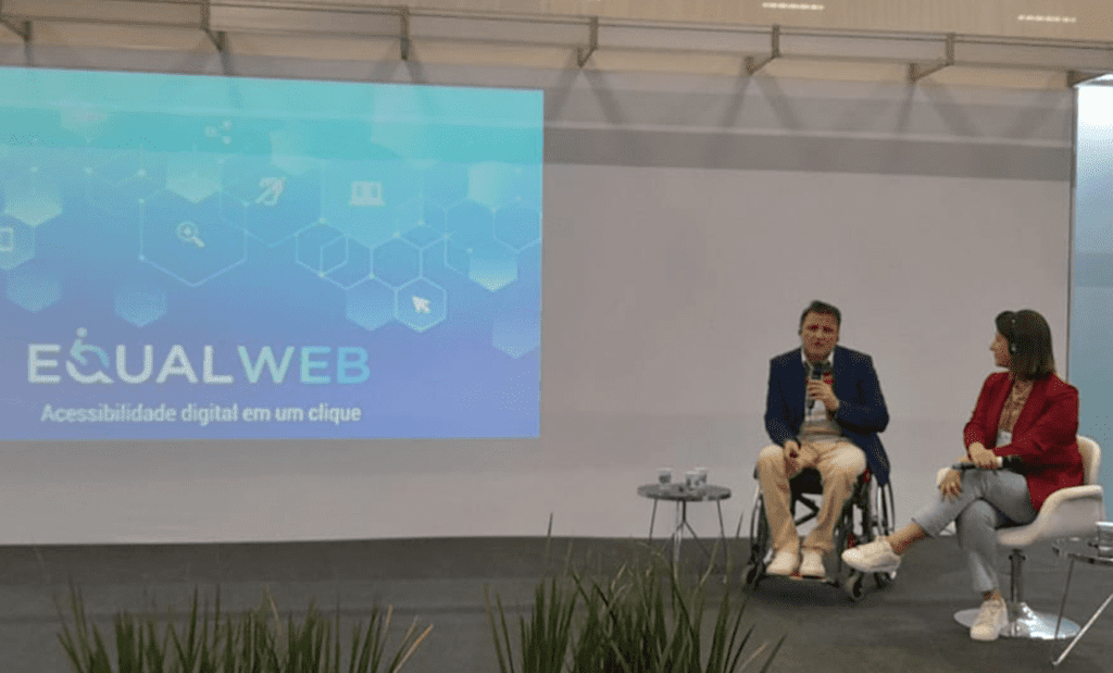 Descrição da imagem: foto da palestra da EqualWeb Brasil na Reatech 2022. Duas pessoas estão no palco. Um homem cadeirante e uma mulher conversam. Ao fundo está um telão com o nome EqualWeb.