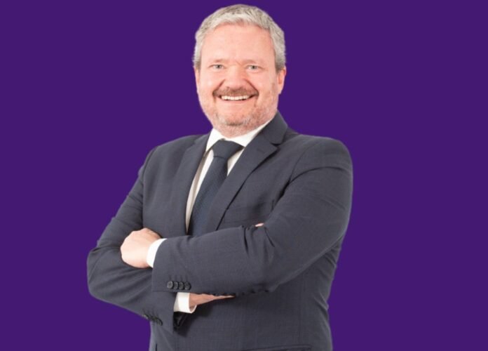 Descrição da imagem: foto do candidato Paullo Vieira. Ele é um homem branco de cabelos e barba grisalhos. Paullo veste um terno preto e está com os braços cruzados. Fim da descrição.