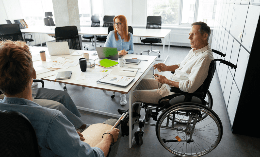 Descrição da imagem: foto de um grupo de pessoas em um ambiente corporativo. Elas estão conversando. Uma das pessoas é cadeirante. Fim da descrição.