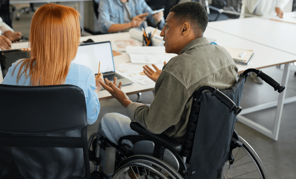 Descrição da imagem: foto de um grupo de pessoas em um ambiente corporativo. Elas estão conversando. Uma das pessoas é cadeirante. Fim da descrição.