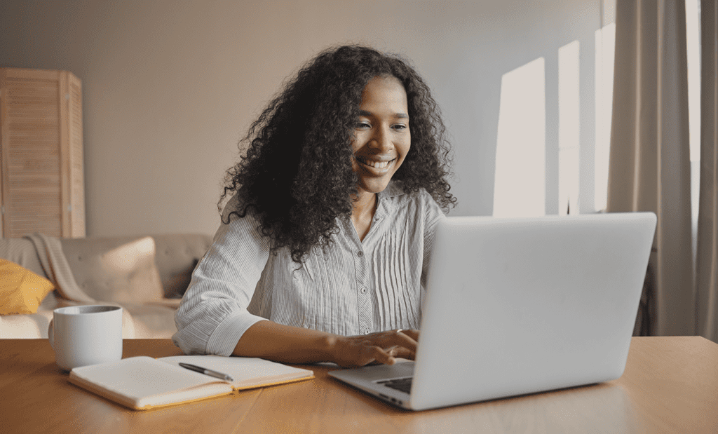 Descrição da imagem: foto de uma mulher usando um notebook. Ela está sorrindo. Fim da descrição.