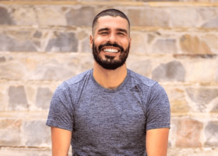 Descrição da imagem: foto do paratleta Daniel Dias. Ele é um homem branco de cabelos castanhos. Daniel tem barba. Ele está vestindo uma camiseta cinza e sorri. Fim da descrição.