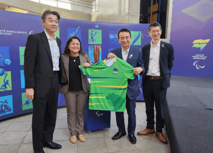 Descrição da imagem: foto da presidente da CBDS, Diana, com representantes da delegação da cidade de Hamamatsu. Ela está ao lado de três homens e eles seguram uma camisa da CBDS. Fim da descrição.