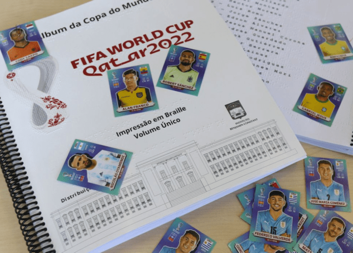 Descrição da imagem: foto do álbum da Copa impresso em braiile com as figurinhas sobre ele. Fim da descrição.