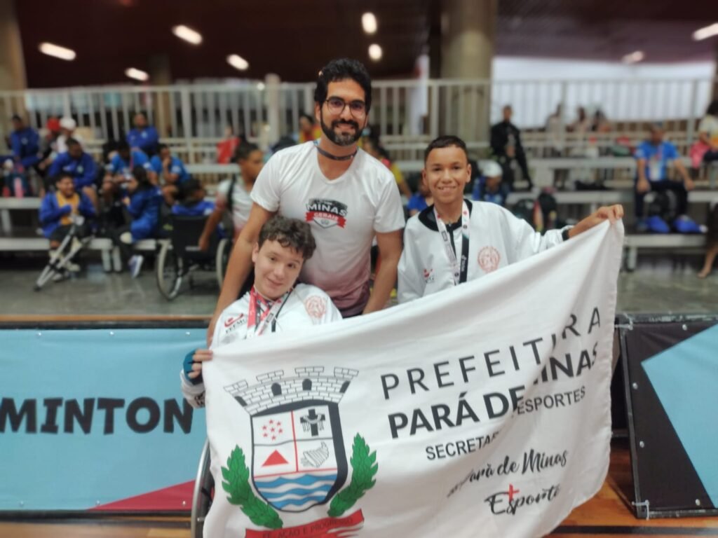 Descrição da imagem: foto do técnico surdo Gabriel com os dois paratletas. Eles estão segurando uma faixa de Pará de Minas. Fim da descrição.