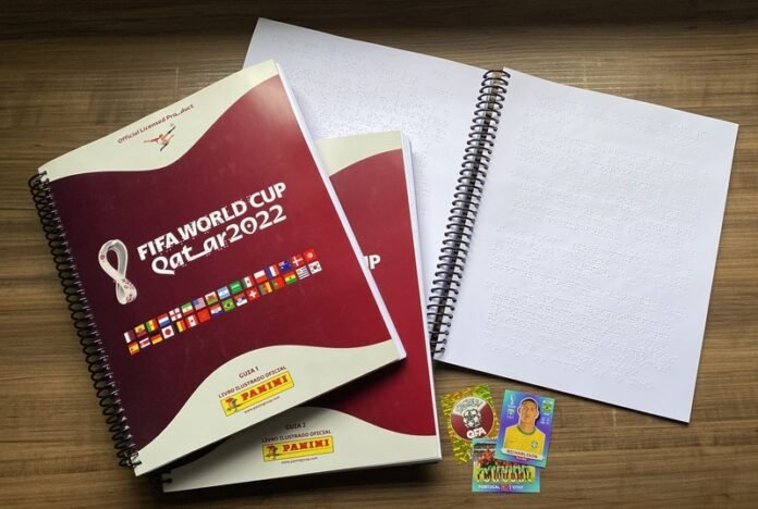 Descrição da imagem: foto do álbum da Copa com as guias e figurinhas em braiile. Fim da descrição.