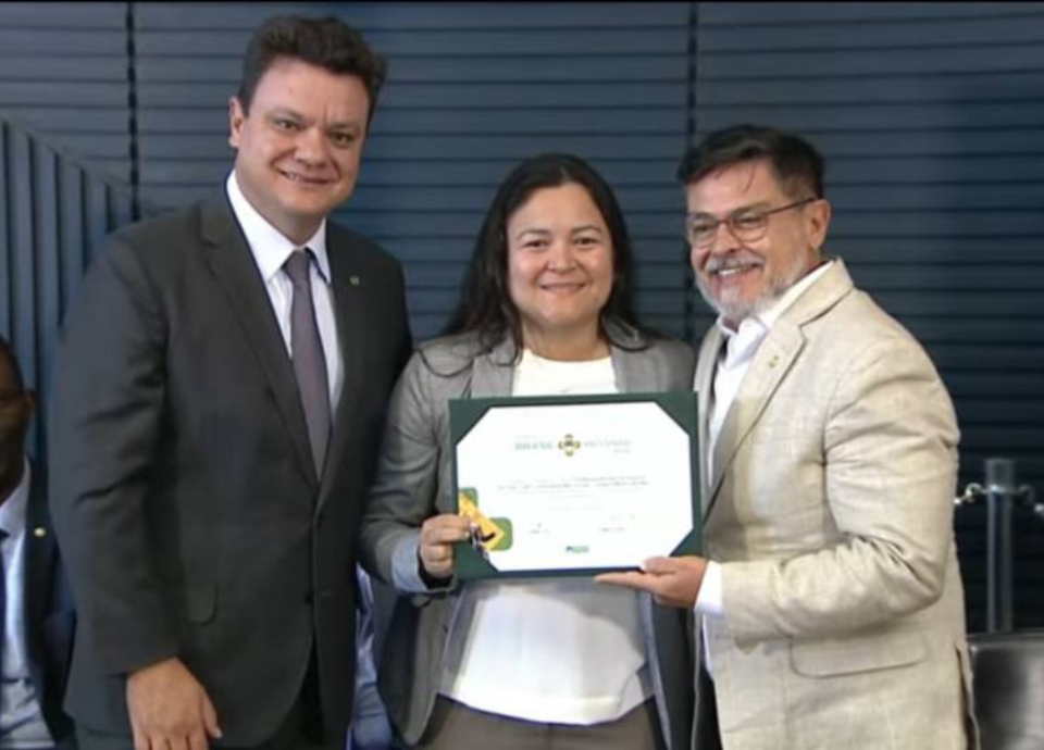 Descrição da imagem: foto de Diana com dois deputados, durante a entrega do diploma. Fim da descrição.