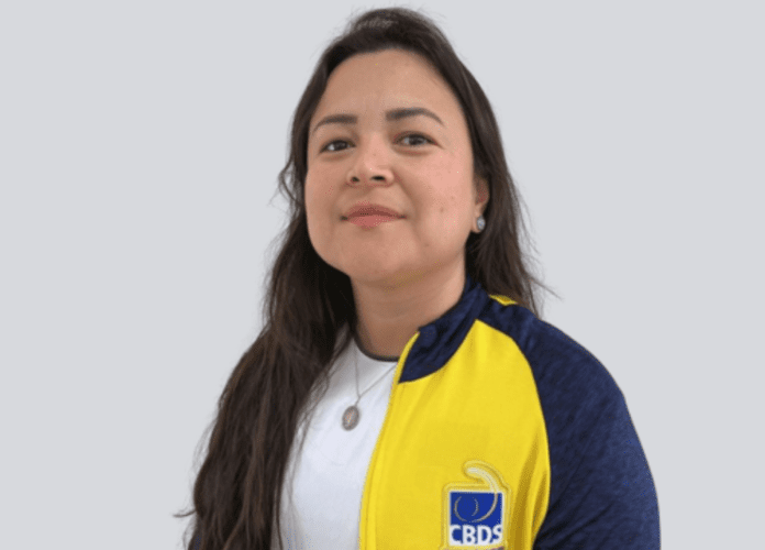Descrição da imagem: foto de Diana Kyosen, presidente da CBDS. Diana é uma mulher com traços orientais. Ela tem cabelos pretos, lisos e compridos. Ela está vestindo uma camiseta branca e um agasalho amarelo e azul da CBDS. Fim da descrição.