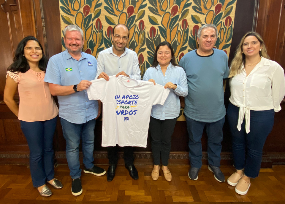 Descrição da imagem: foto da equipe da CBDS na Secretaria de Esportes do Estado de São Paulo. Eles estão segurando uma camiseta branca com a frase: eu apoio o esporte para surdos. Fim da descrição.