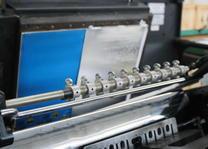 Foto de uma máquina da gráfica braille da Fundação Dorina. A imagem registra o momento em que uma impressão em braille está sendo feita. Fim da descrição.