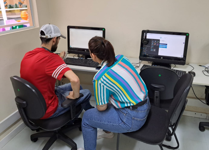 Descrição da imagem: foto de duas pessoas sentadas usando o computador. Uma delas tem deficiência visual e está realizando o cadastro no portal de empregabilidade, com a ajuda de uma profissional da fundação. Fim da descrição.