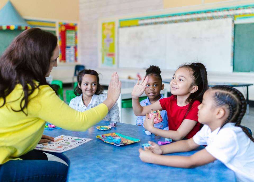 #descricaodaimagem foto de uma educadora com seus alunos em uma sala de aula. Fim da descrição.