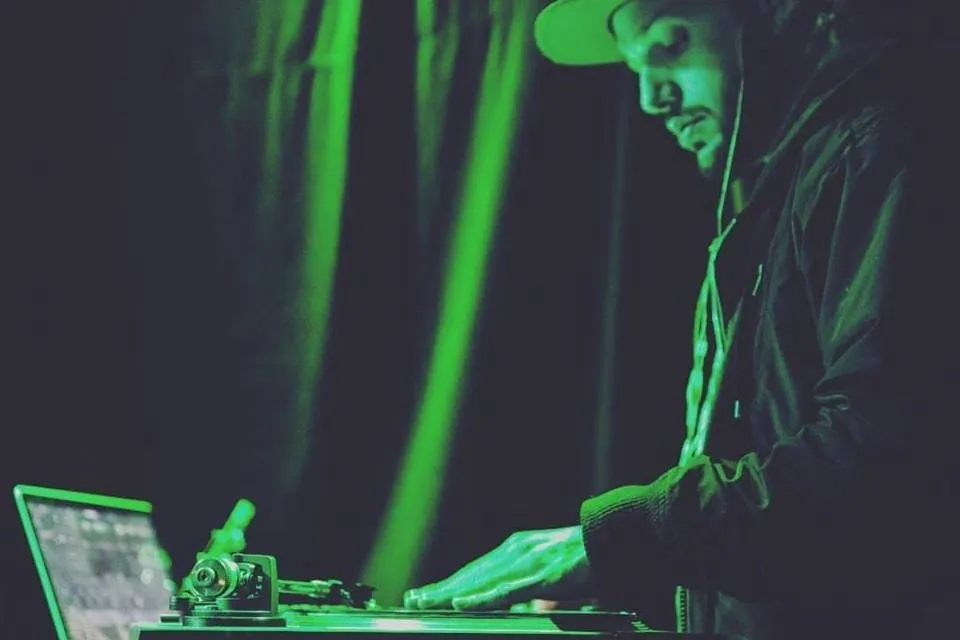#descricaodaimagem o DJ Robbie Wilde durante discotecagem. A imagem tem uma luz verde. Fim da descrição.