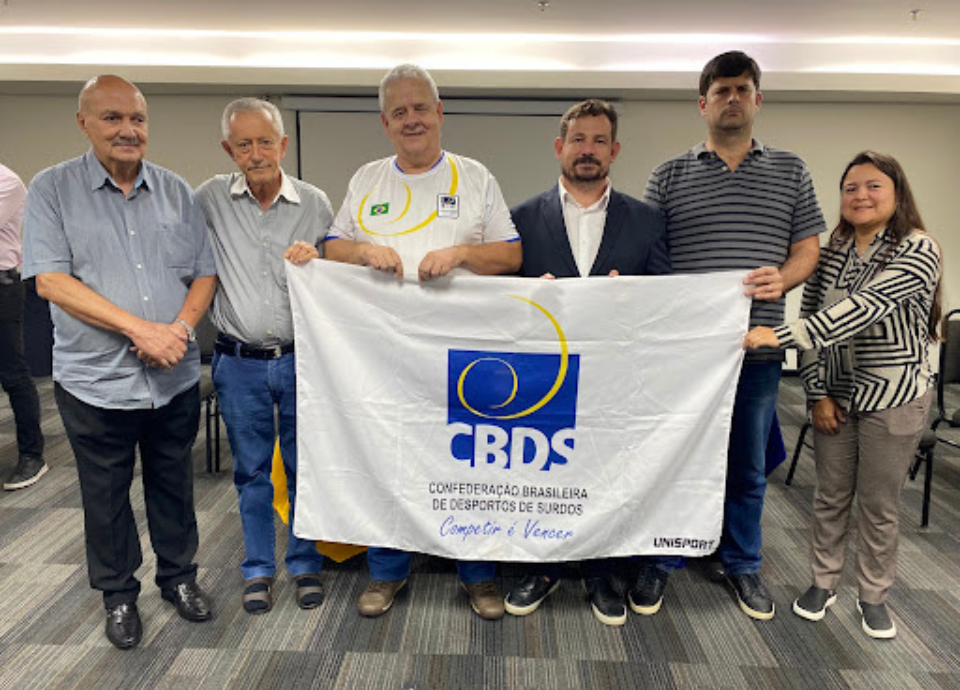 #descricaodaimagem foto dos ex-presidentes com a atual presidente da CBDS. Eles seguram a bandeira da CBDS. Fim da descrição.