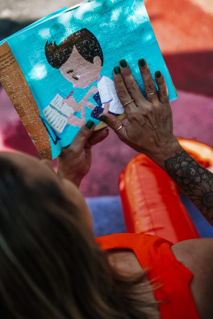 #descricaodaimagem #pratodosverem foto de uma mulher tocando a página do livro, que traz acessibilidade em braile.
