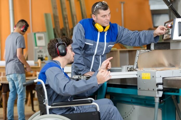 #descricaodaimagem #pracegover foto de dois homens trabalhando em uma indústria. Um deles é cadeirante.