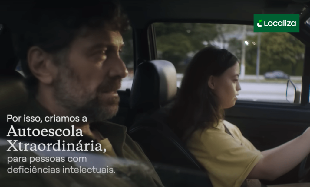 #descriçãodaimagem #pratodosverem imagem de uma campanha publicitária da empresa Localiza. Nela estão duas pessoas, em um carro. São elas um homem, no banco do passageiro, e uma mulher com síndrome de Down, que está ao volante. No canto inferior esquerdo está a seguinte frase: Por isso, criamos a Autoescola Xtraordinária, para pessoas com deficiências intelectuais.