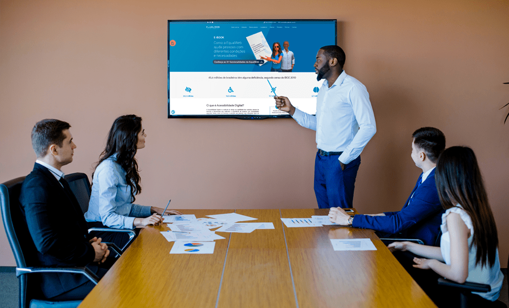 #descricaodaimagem #pratododverem foto de uma sala de reuniões com algumas pessoas e uma delas está apresentando o site da Equalweb para o restante do grupo.