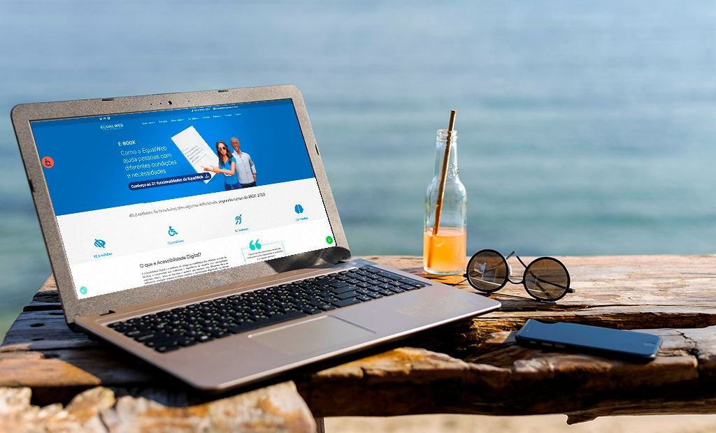 #descricaodaimagem #pratodosverem foto de um notebook aberto sobre uma mesa, na beira do mar. Na tela do notebook está aberta a página do site da EqualWeb Brasil.