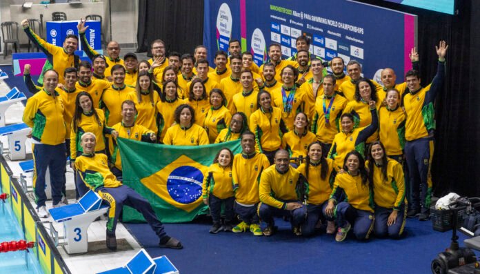 #descricaodaimagem #pratodosverem foto dos atletas que participaram do Mundial de Natação Paralímpica. Todos estão usando um agasalho amarelo e, alguns atletas, seguram a bandeira do Brasil.