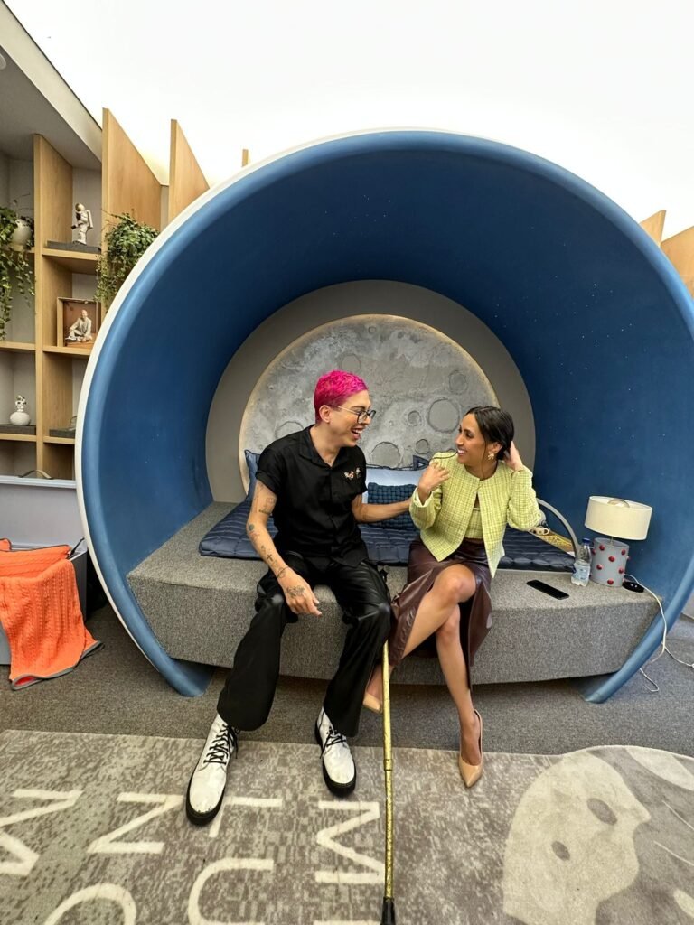 #descricaodaimagem #pracegover foto de Ivan Baron com a arquiteta Rafaela Bruna. Eles estão sentados na cama do ambiente, projetado em homenagem a Ivan. Eles estão conversando.
